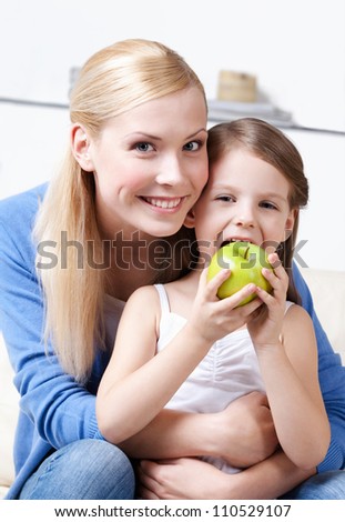 Smiley mum with her eating green apple daughter