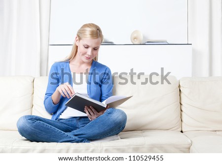 Woman reads the book lying on the white leather sofa