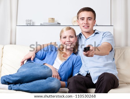 Sitting on the white couch married couple is going to watch TV set