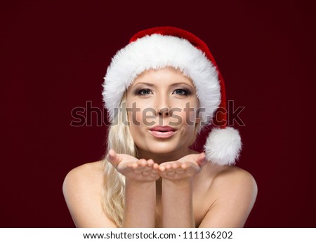 Attractive woman in Christmas cap blows kiss, isolated on purple