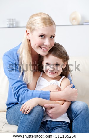 Smiley mother hugs her daughter on the sofa