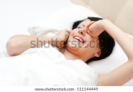 Woman in underwear speaks on cellular while lying in the bed, white background