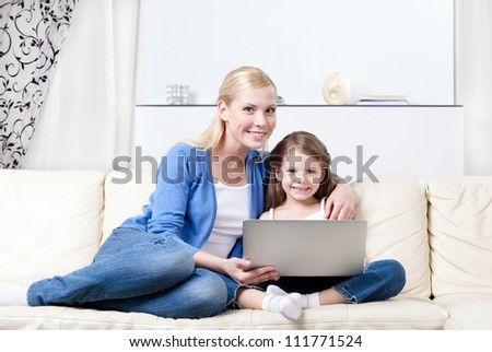 Little child surfs on the internet with her mom sitting on white sofa