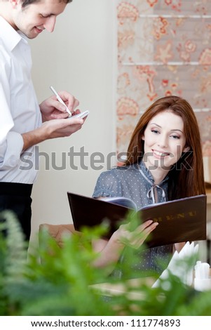 Woman makes an order. The waiter listens to her attentively and white down everything