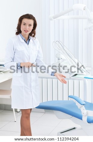 Beautiful doctor\'s assistant shows the dentist\'s chair and explain its work