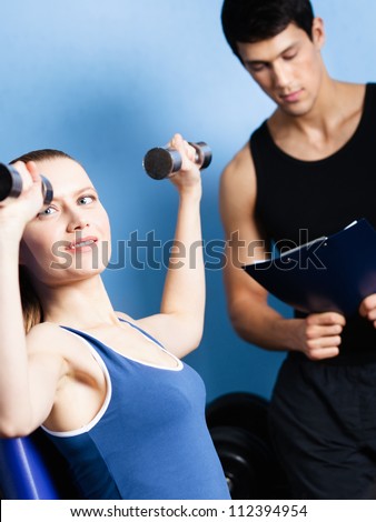 Coach controls sports actions of pretty woman working out with dumbbells in fitness gym