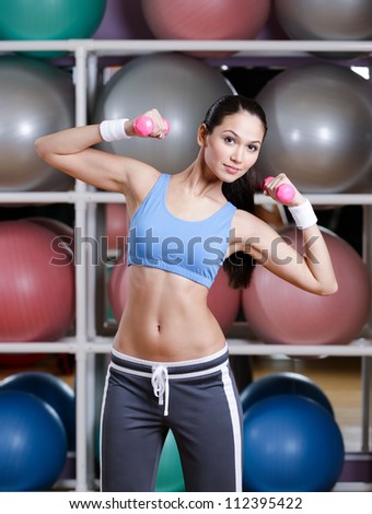 Young woman training with dumbbells in gym to develop muscular system. Strength