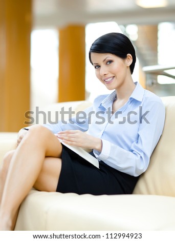 Successful young business woman rests at the sofa reading book at the hall