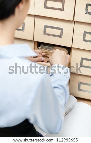 Woman searches something in card catalog composed of set of wood boxes at the library. Education and research