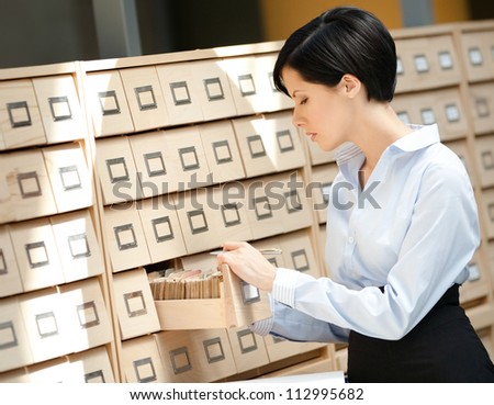 Woman seeks something in card catalog composed of set of wood boxes at the library. Education and research