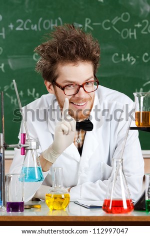 Mad professor surrounded with chemical glassware shows forefinger in his laboratory