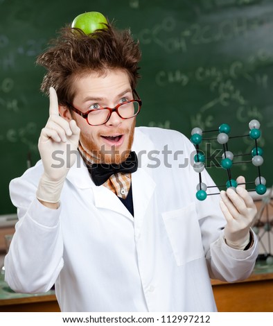 Mad scientist with a green apple on his head shows forefinger while handing molecular	model
