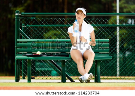 Female tennis player rests with bottle of water on the bench at the tennis court