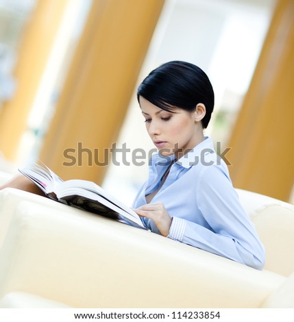 Business woman rests at the white sofa reading book at the hall