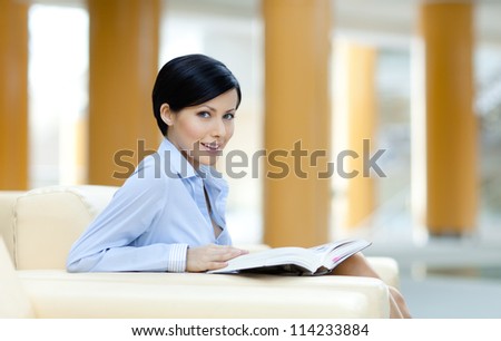 Business woman sits at the sofa reading book at the hall