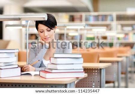 Beautiful student studies with piles of books at the reading hall