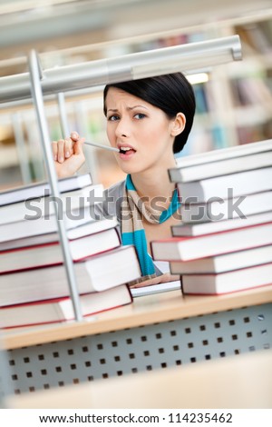 Sitting at the desk student surrounded with piles of books are in panic. Learning process