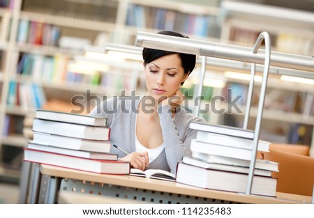 Woman surrounded with piles of books reads sitting at the desk at the reading hall. Information concept