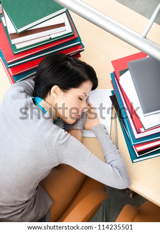 Female student sleeping at the desk with piles of books. Tired of learning. Top view