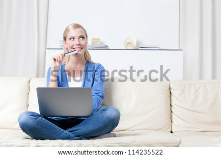 Young girl thinks about purchasing through the internet sitting on the sofa