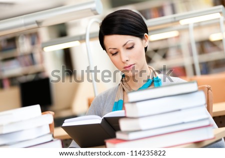 Woman surrounded with piles of books reads sitting at the desk at the library. Academic achievement