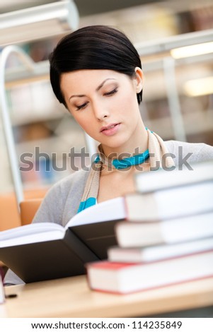 Woman surrounded with piles of books reads sitting at the table at the reading hall. Knowledge concept