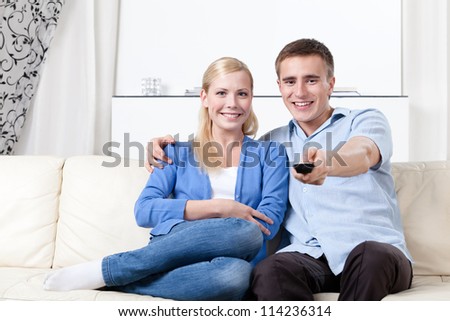 Sitting on the white leather sofa couple is going to watch TV set