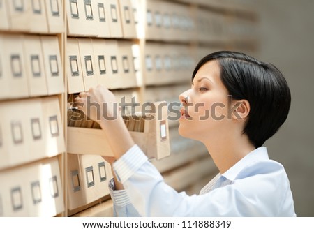Woman searches something in card catalog composed of set of wood boxes at the library. Information