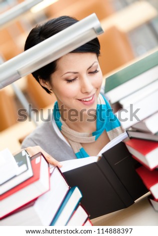 Reading book female student surrounded with piles of books sitting at the desk at the library. Knowledge concept