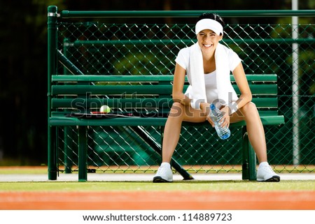 Tennis player rests with bottle of water on the bench at the tennis court