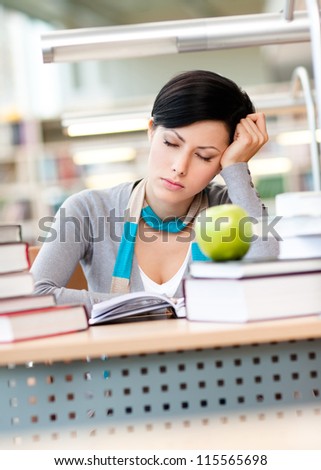 Female student with green apple sleeps sitting at the desk at the reading hall of the library. Data concept
