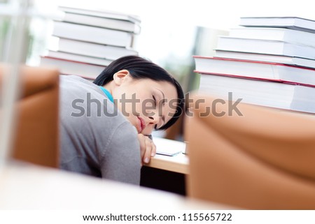 Tired female student surrounded with piles of books sleeps at the desk at the library