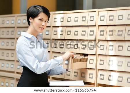 Pretty woman searches something in card catalog composed of set of wood boxes at the library. Studying