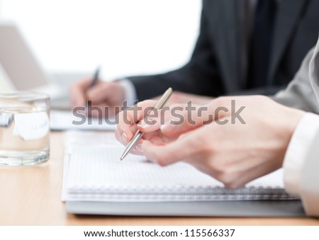 Business people writing in notebooks sitting at the office table. Close up of hands