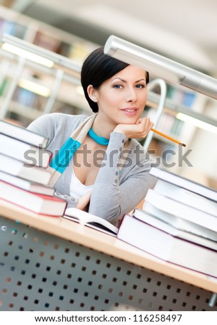 Pretty student studies with piles of books sitting at the table at the reading hall