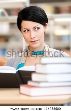 Woman surrounded with piles of books reads sitting at the table at the reading hall. Learning process
