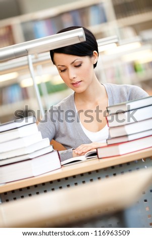 Woman surrounded with piles of books reads sitting at the desk at the library. Knowledge concept