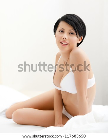 Halfnaked woman sits on the bed with white bed linen