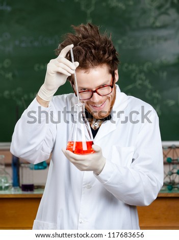 Mad professor adds something to the flask with red liquid in his laboratory