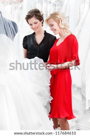 Girl hesitates about wedding gown. Shop assistant advises the client to select a proper dress