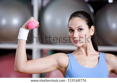 Sportswoman training with dumbbells in gym. Physical strength and developing muscles