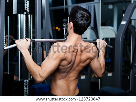 Athletic young man works out on training apparatus in fitness gym