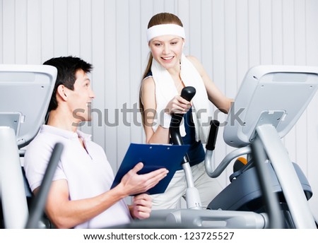 Young woman training on gym training in gym with coach writing down the results