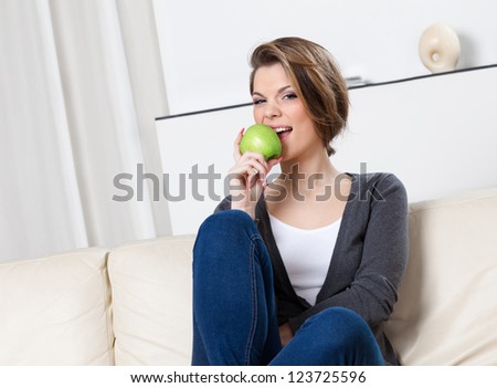 Sitting on the sofa attractive woman eats a green apple