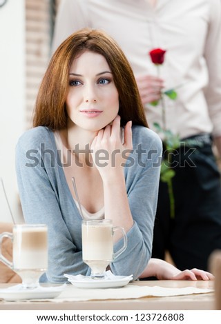 Woman at the coffee house and man with rose behind her