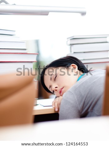 Tired female student surrounded with piles of books sleeps at the table at the library