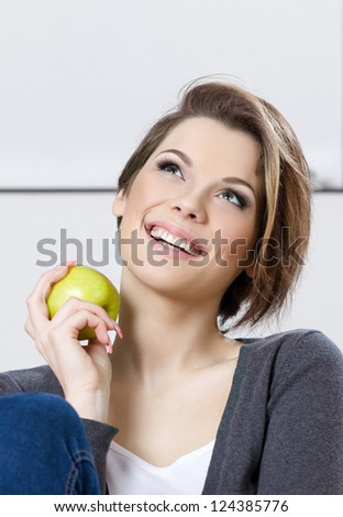 Sitting on the sofa woman eats a green apple
