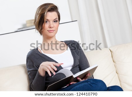 Woman reads the book sitting on the white leather sofa