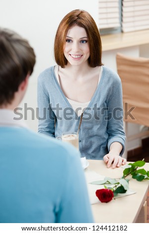 Man and woman are at the cafe table with rose near them