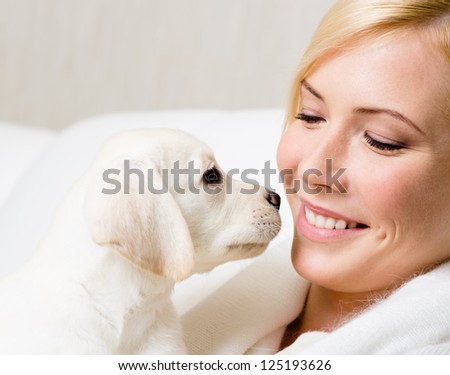 White Labrador puppy and woman sitting at the white leather sofa look at each other